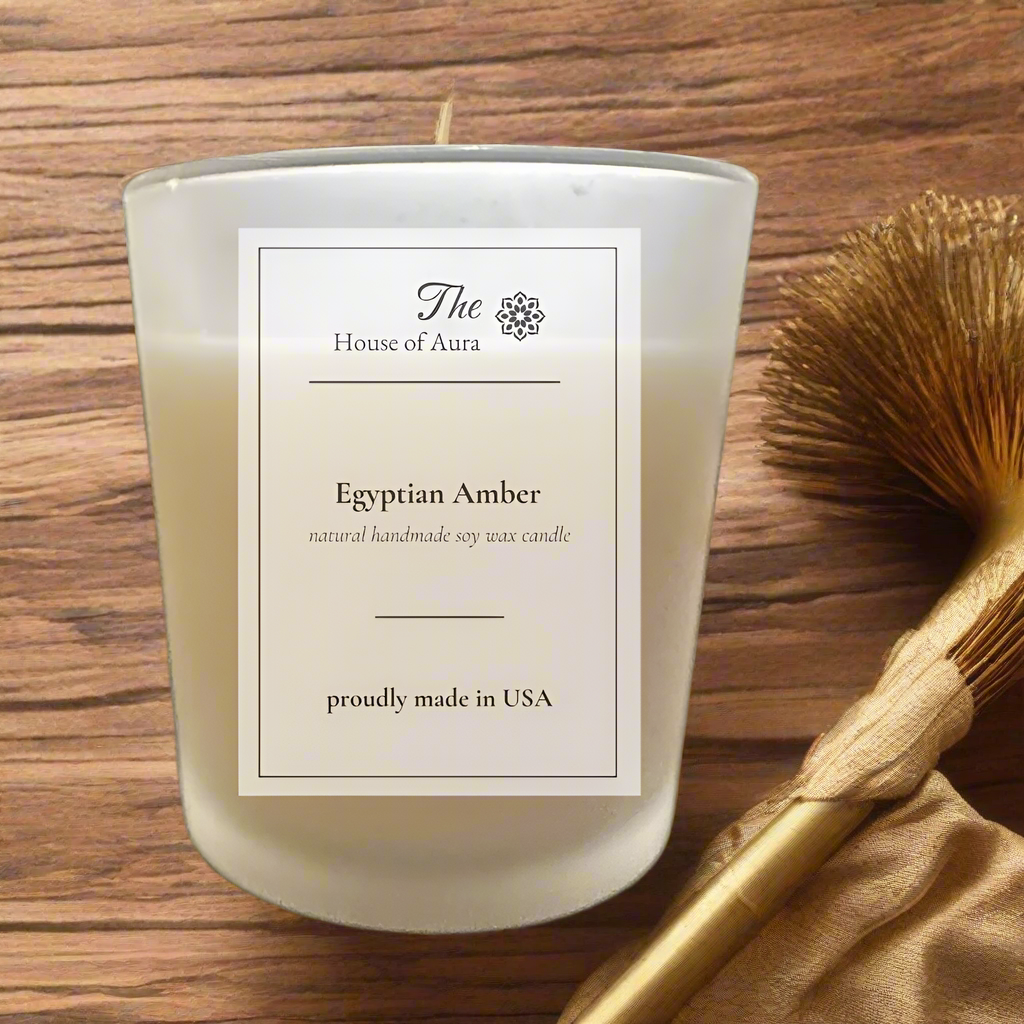 Egyptian Amber soy candle in a frosted glass jar with wooden lid, styled on a dark wood surface with amber accents and warm golden lighting. Handmade by The House of Aura.