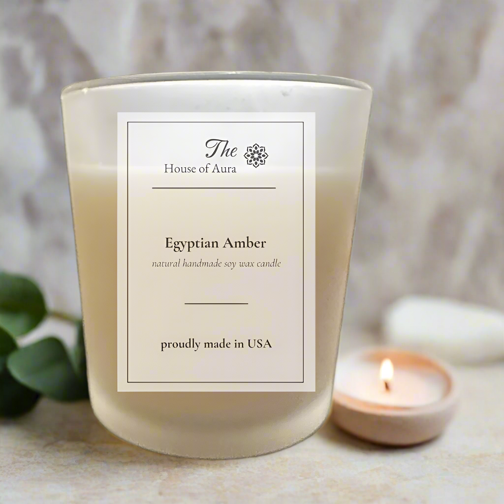 Egyptian Amber soy candle in a frosted jar with wooden lid, styled on a stone surface with dried eucalyptus, a towel, and warm natural light. Handmade by The House of Aura.